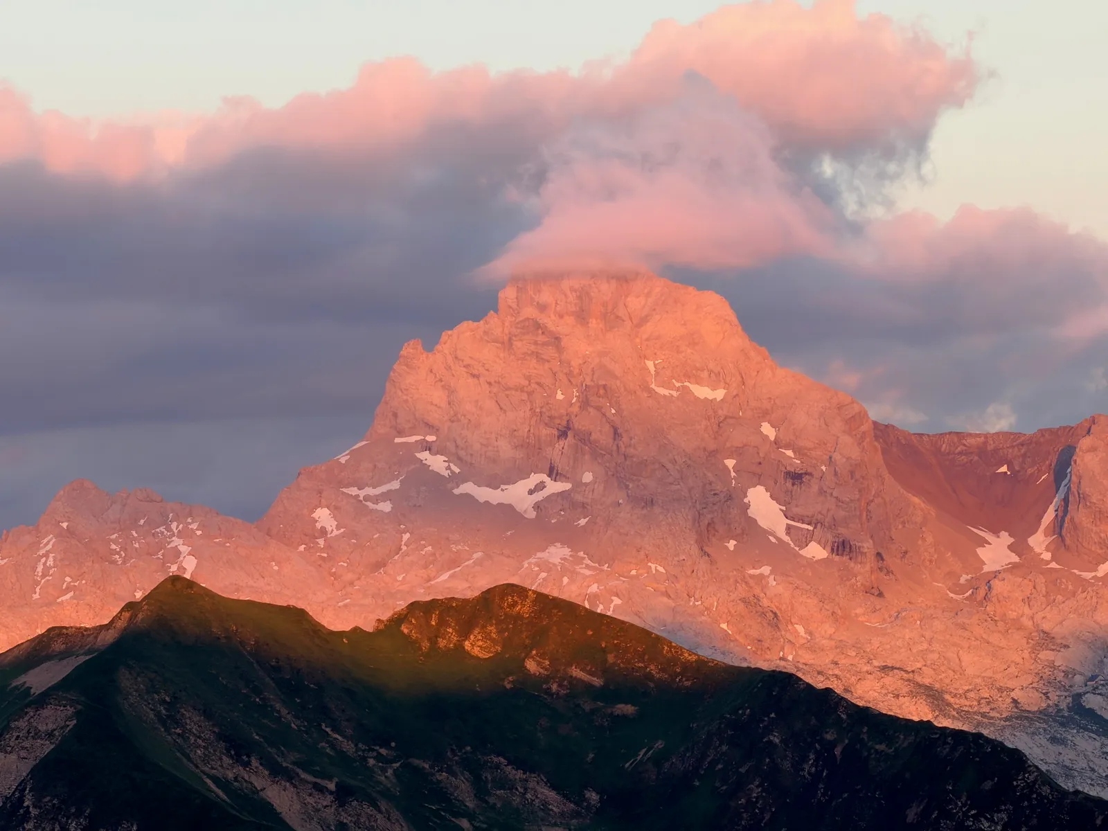 Sommet rocheux et nuages colorés en rose par la lumière du soir.