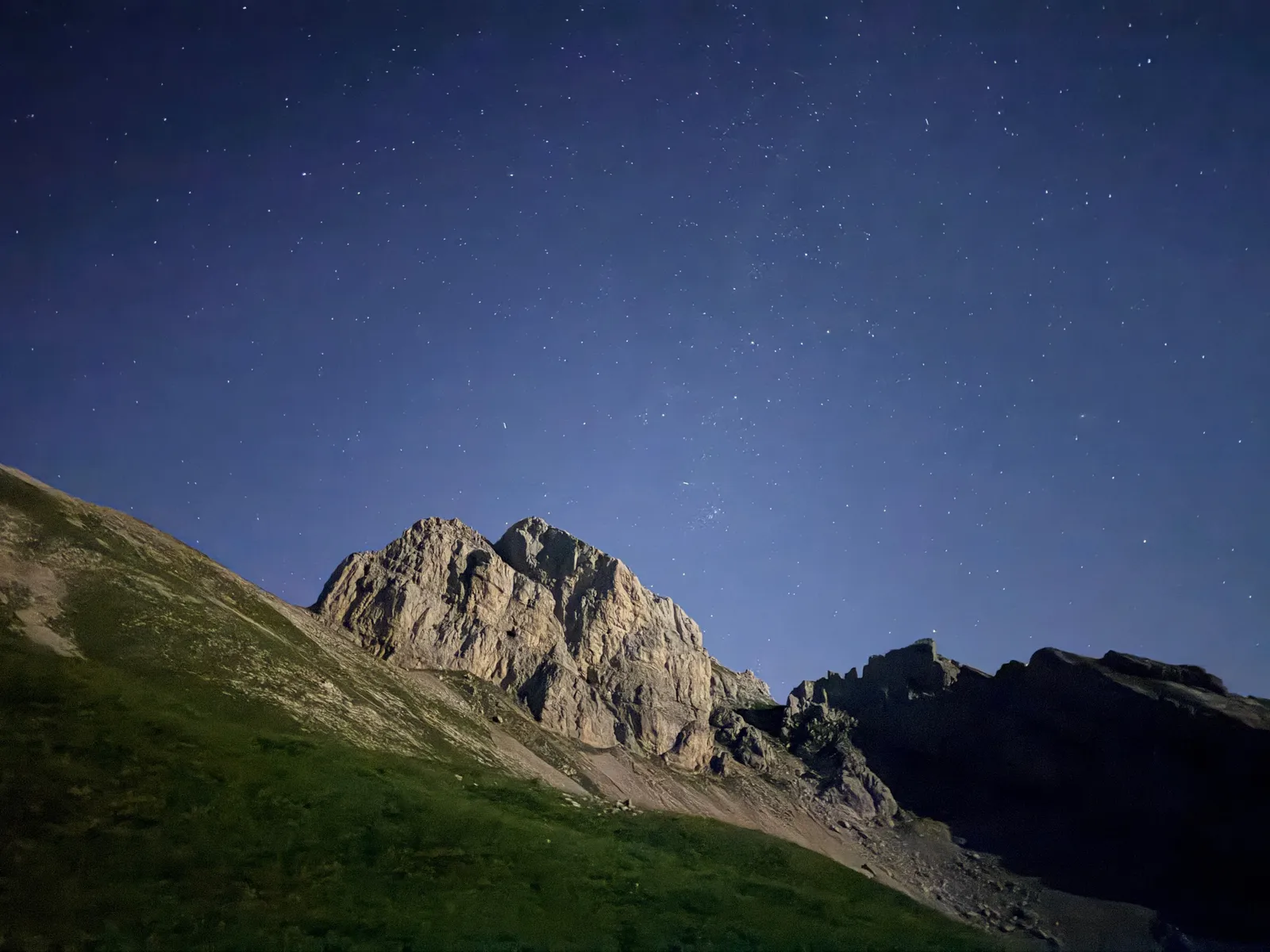 Étoiles au-dessus d’une paroi calcaire et d’un versant herbeux.