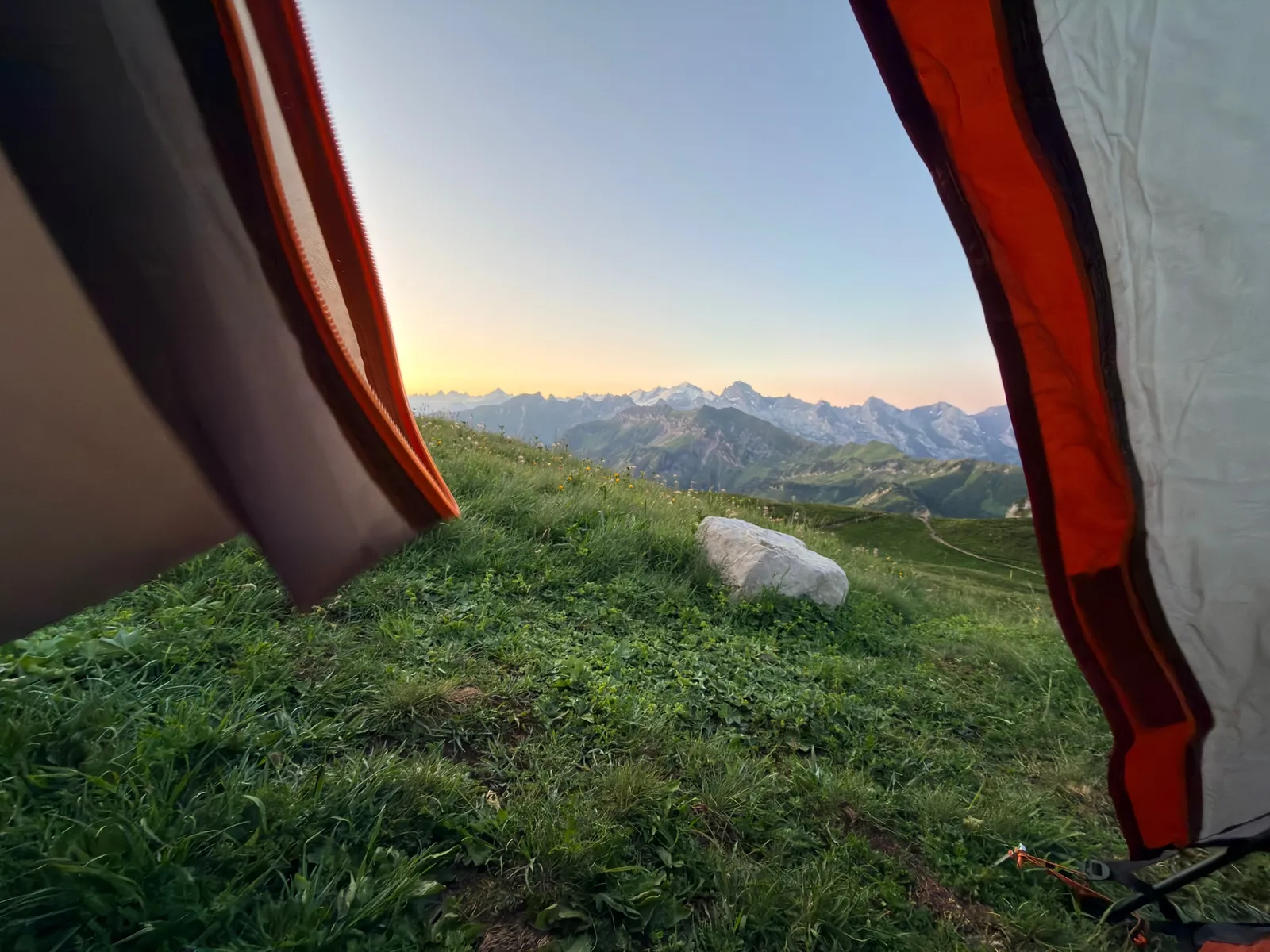 Vue sur les alpages et les montagnes à l’aube depuis l’ouverture d’une tente.