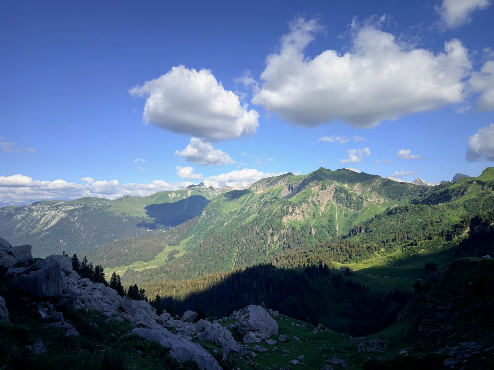 Vallée boisée et crêtes verdoyantes sous les nuages depuis la montée au lac de Peyre.