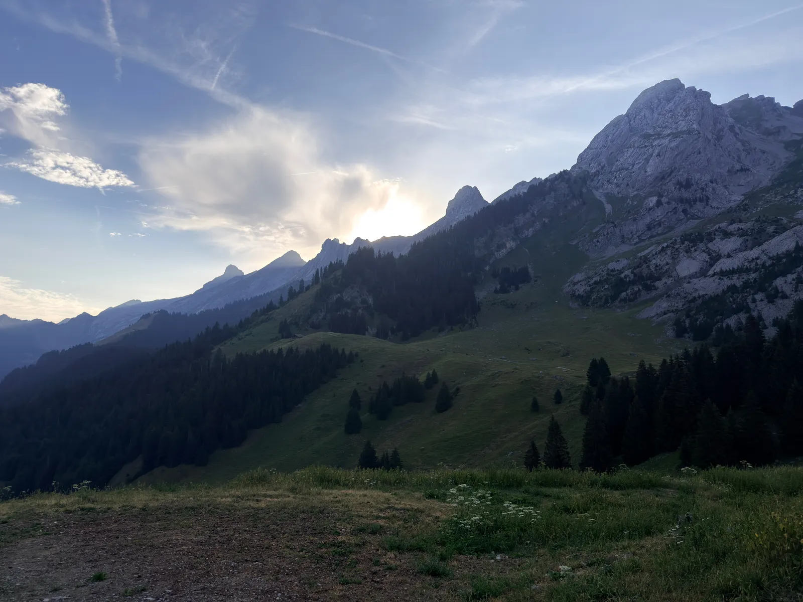 Lumière du matin derrière les crêtes des Aravis au-dessus des alpages et des conifères.