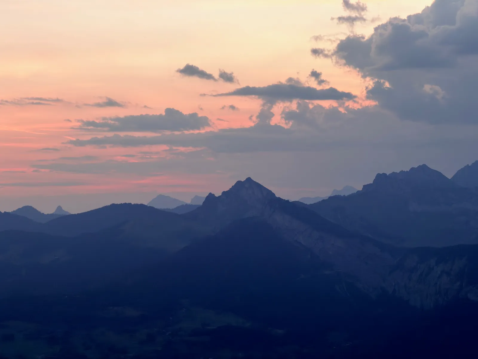 Silhouettes de montagnes sous un ciel rose et orangé avant le lever du soleil.