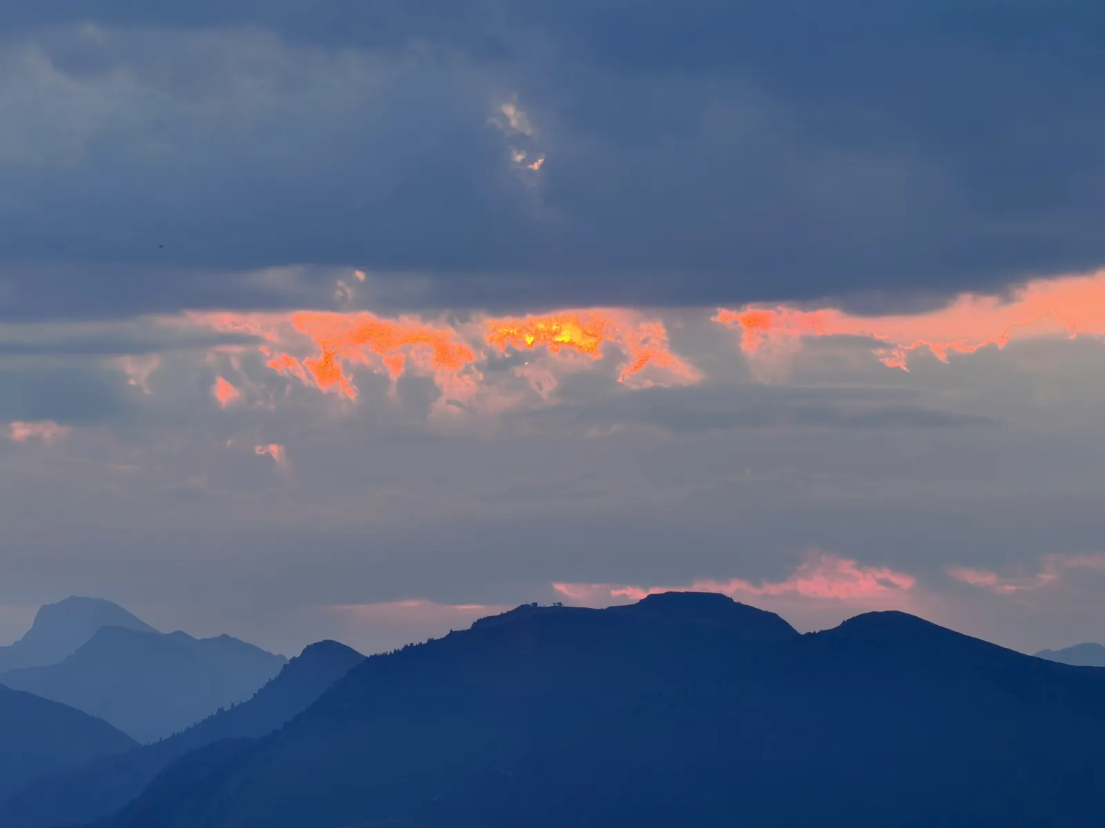 Nuages éclairés en orange au-dessus d’une crête sombre.