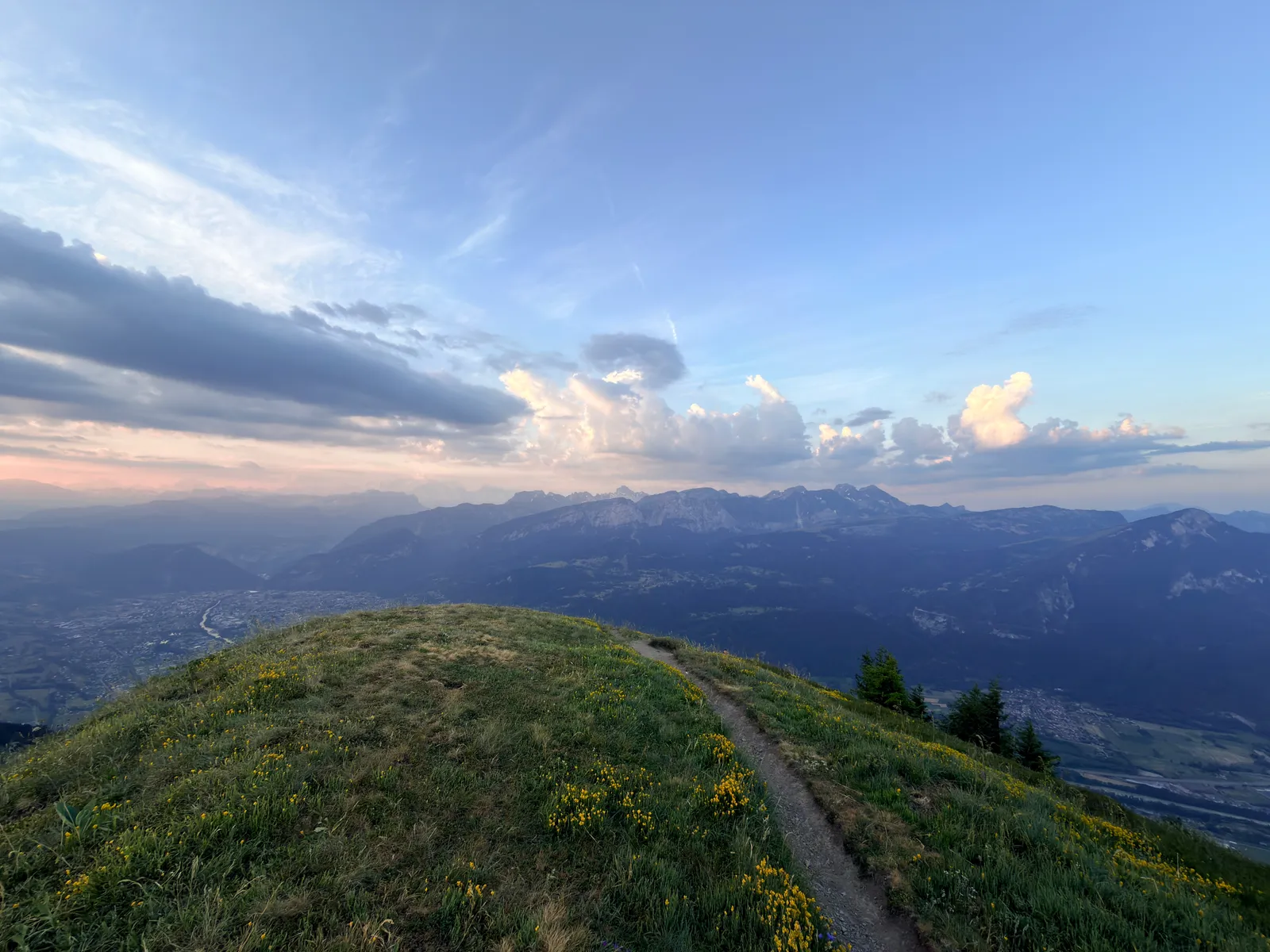 Sentier sur une crête herbeuse du Môle, avec les montagnes et un ciel nuageux en arrière-plan.
