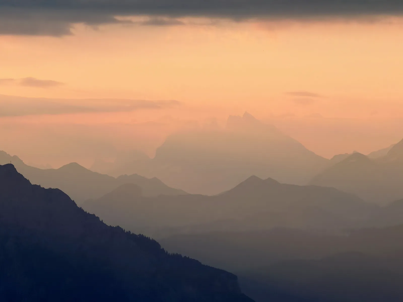 Plans successifs de montagnes dans la brume sous une lumière orangée.