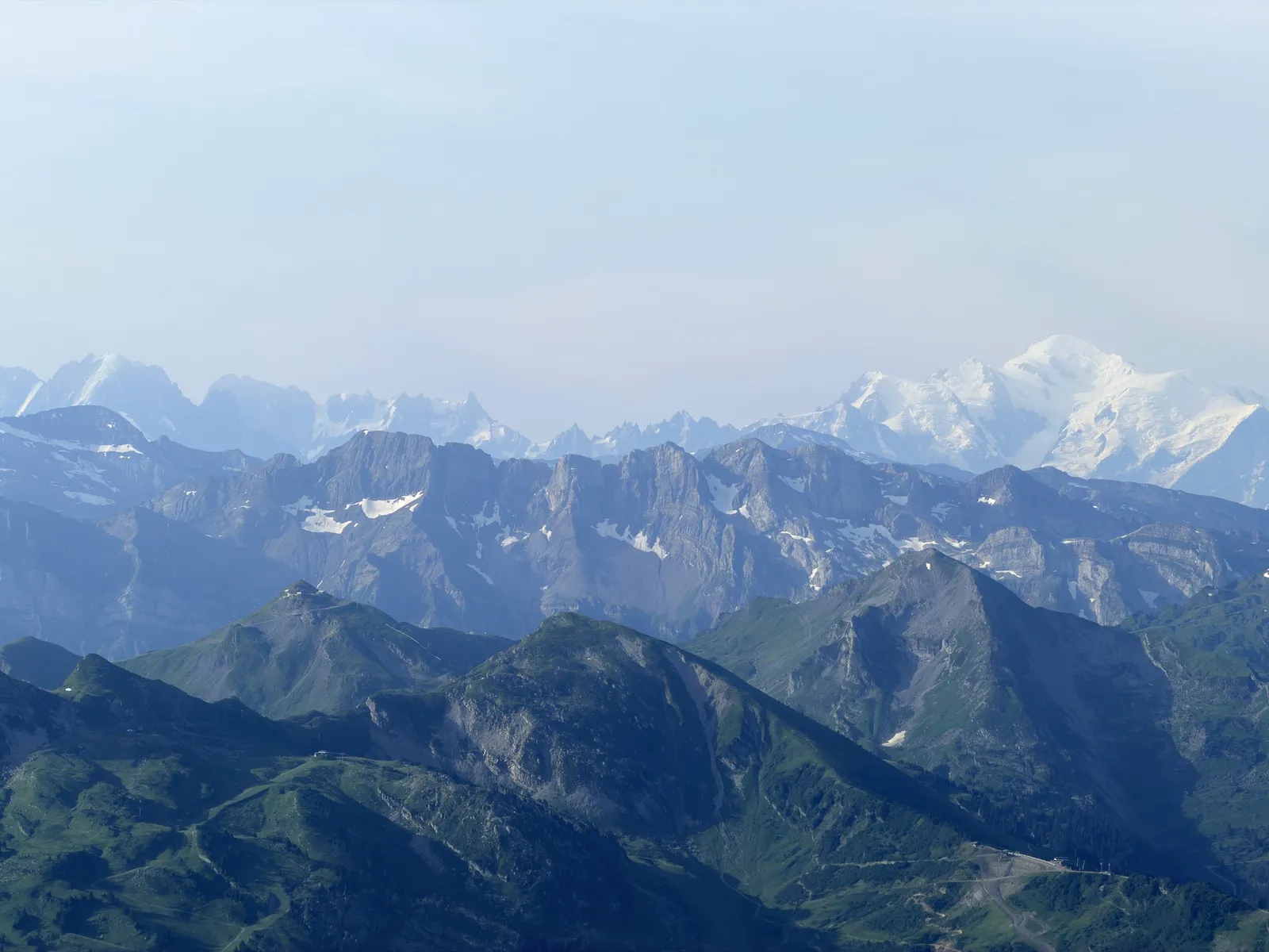 Massif du Mont-Blanc enneigé derrière les crêtes et les alpages.