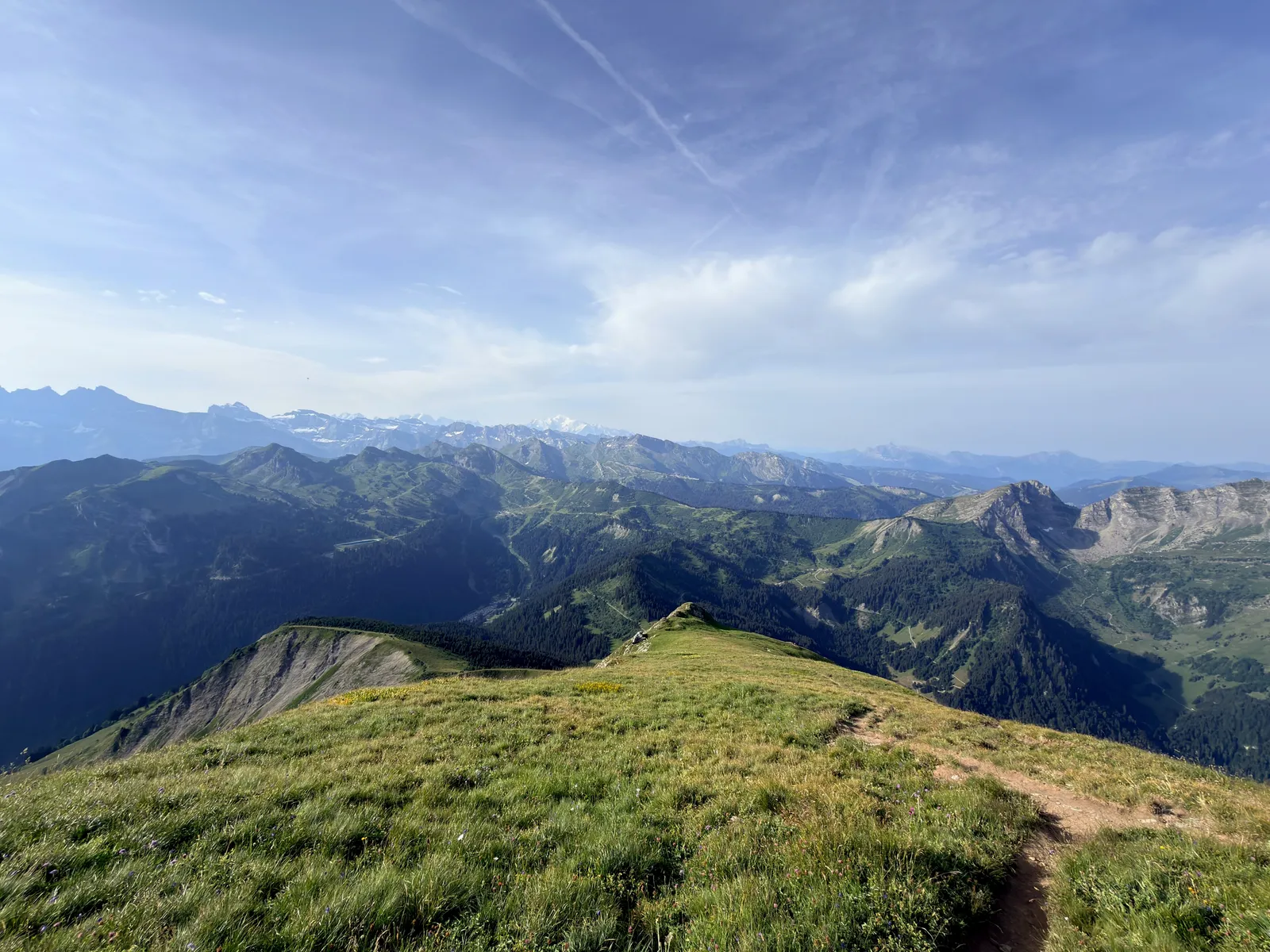Sentier descendant une crête herbeuse face aux montagnes.