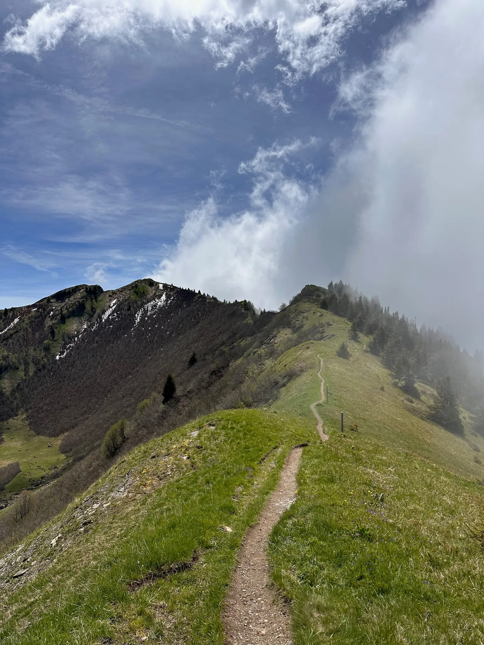 Sentier sur une crête herbeuse bordée de nuages.