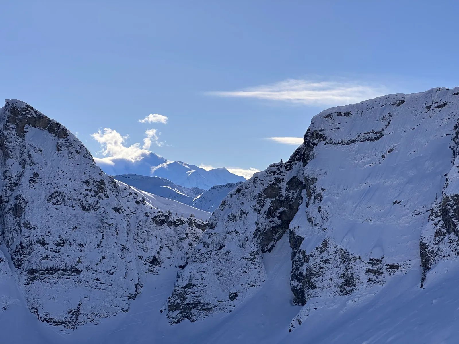 Vue entre deux parois rocheuses enneigées vers les montagnes au loin.