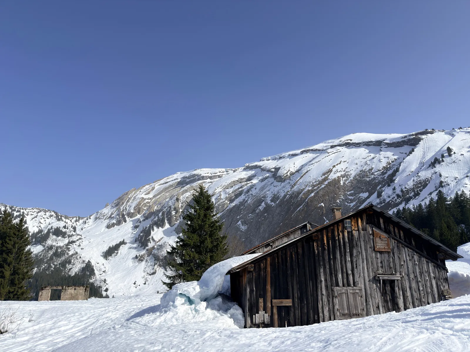 Chalet en bois sous les falaises enneigées sur le parcours de Bostan