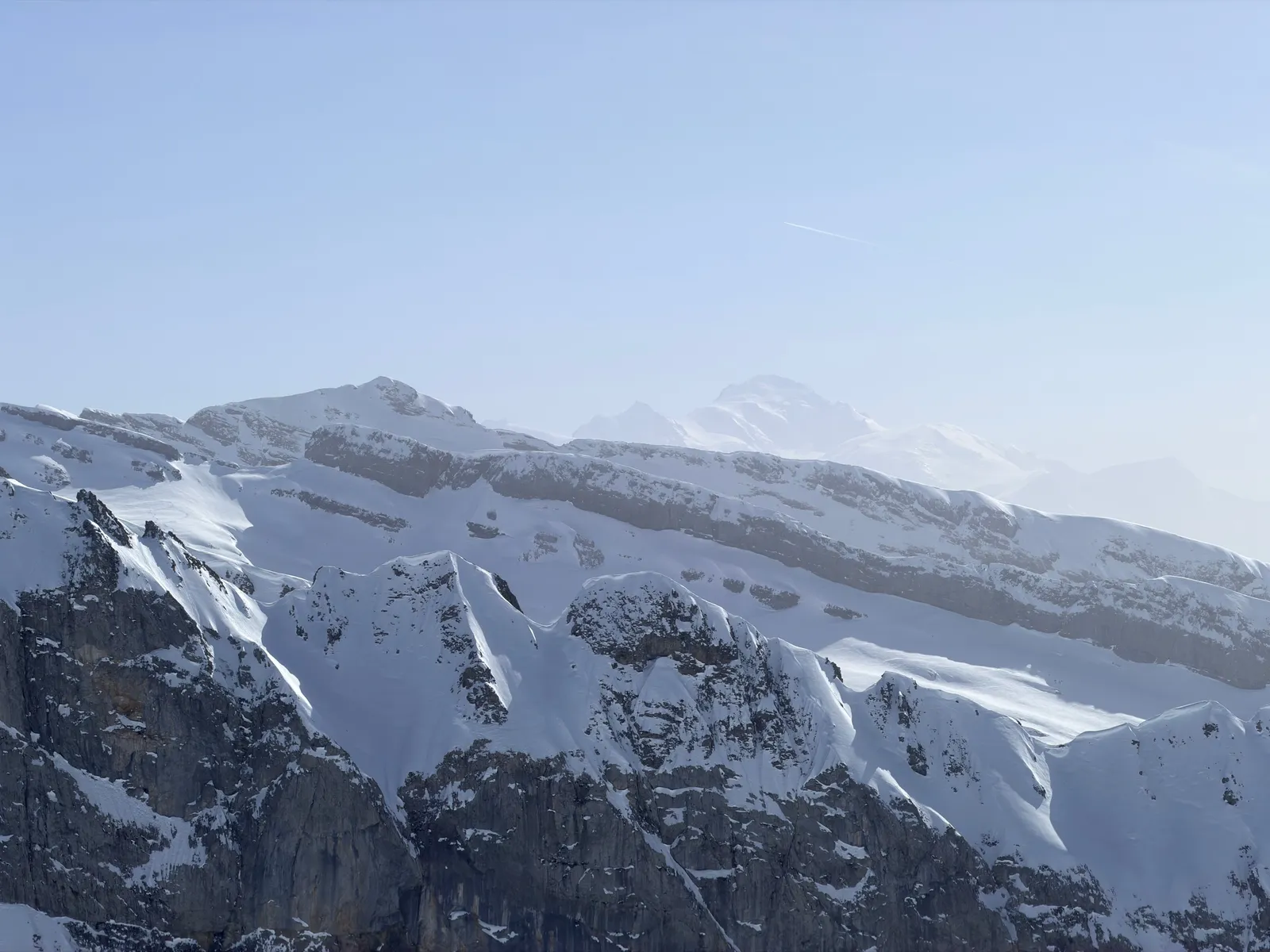 Parois et corniches enneigées avec le Mont-Blanc en arrière-plan dans la brume.